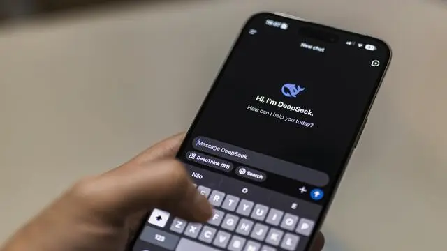 A person holding a smartphone with the DeepSeek AI chat interface open, displaying the message 'Hi, I'm DeepSeek. How can I help you today?' on a dark screen.