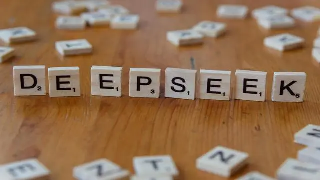 Scrabble tiles spelling 'DeepSeek' on a wooden table, with scattered pieces in the background.